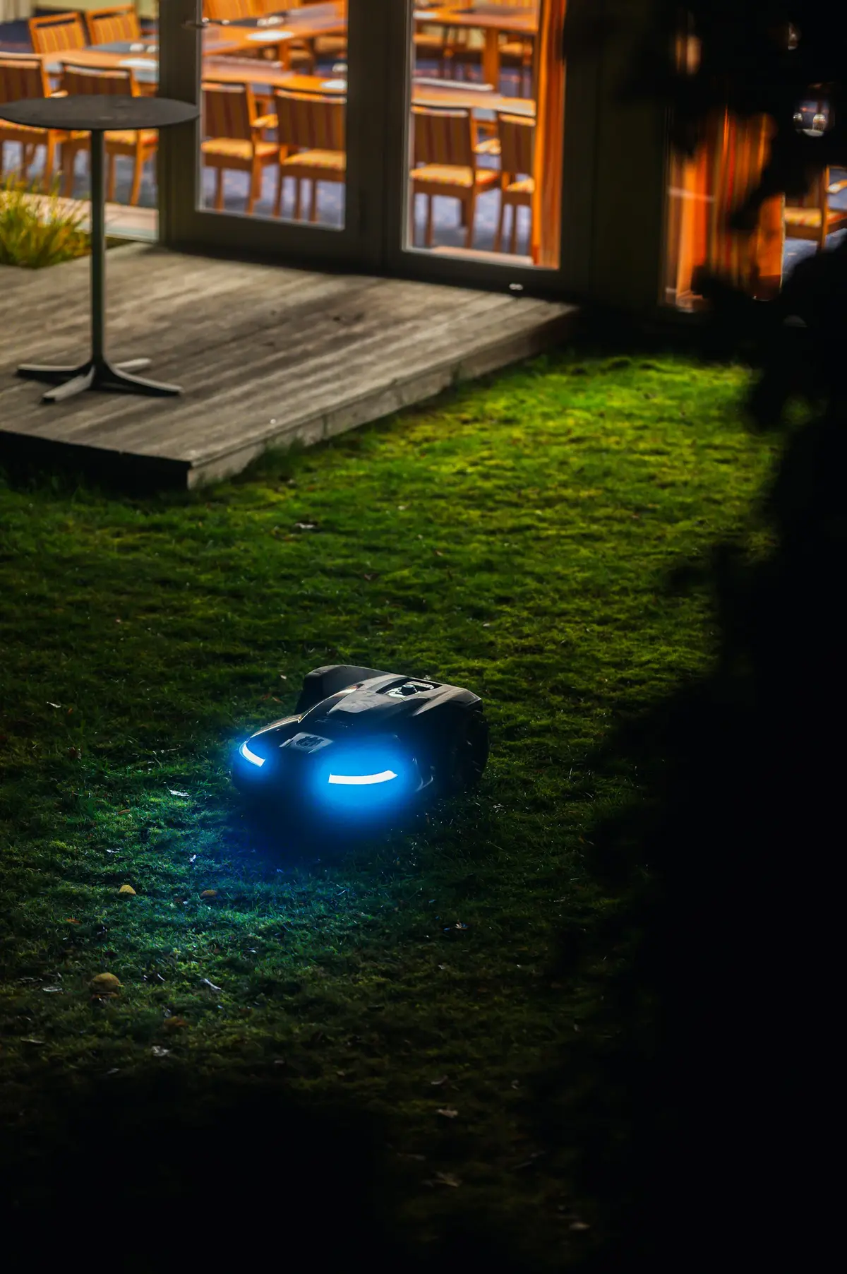 Robotmaaier op een gazon naast een terras, in de avond